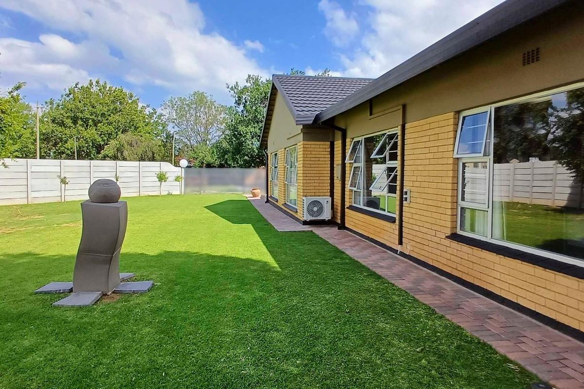 Rear view of the property featuring a well-maintained lawn, paved walkway, brick facade, and secure precast boundary walling.