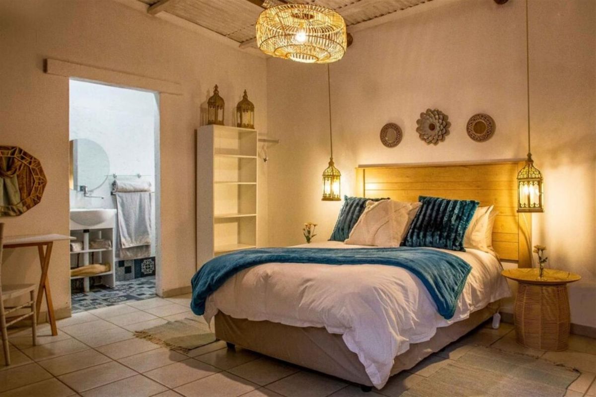 A cozy bedroom featuring a wooden headboard, tiled flooring, and an adjoining en-suite bathroom with a vanity and patterned floor tiles.