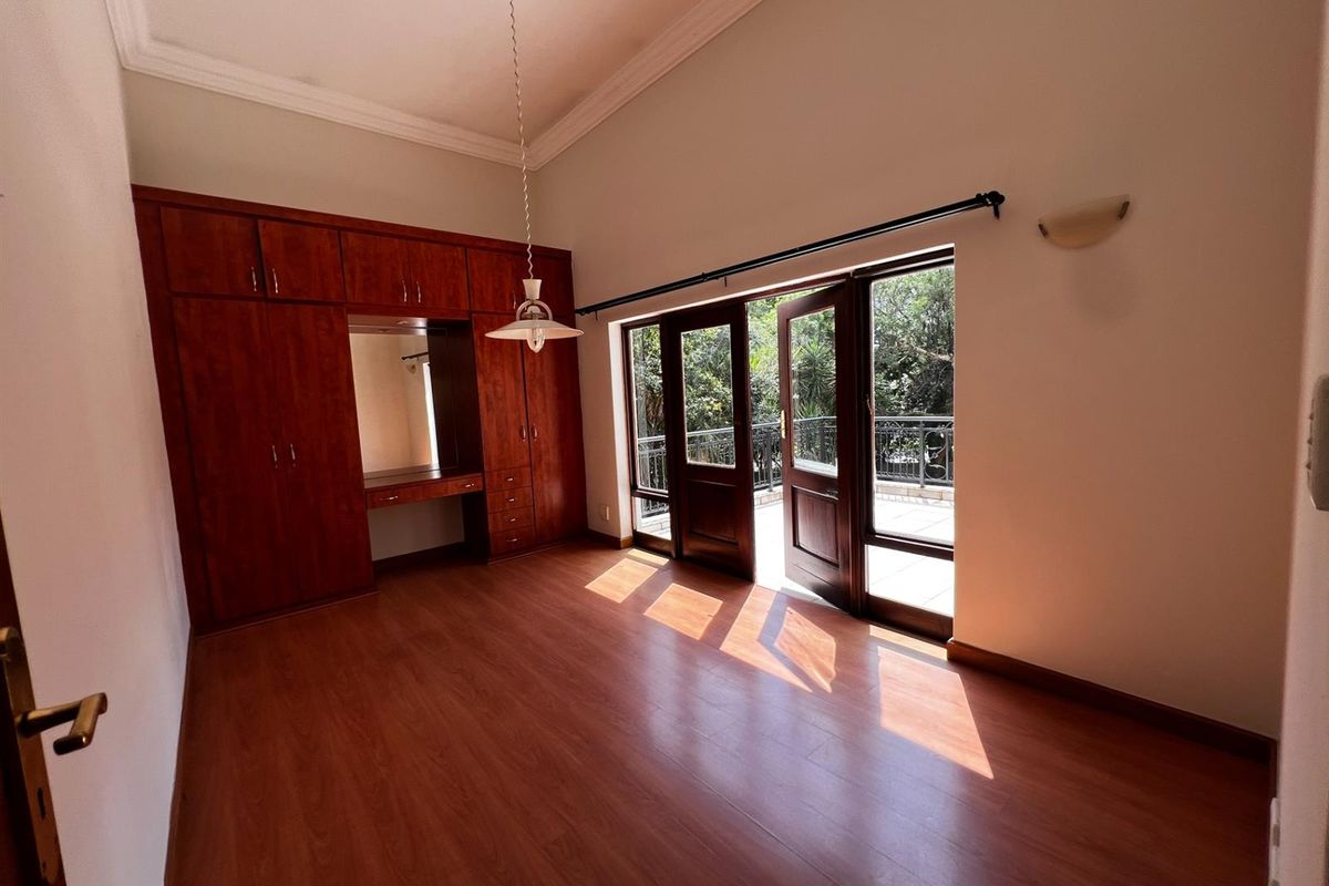 Spacious bedroom featuring built-in wooden cabinetry, laminate flooring, and double doors opening onto a private balcony with garden views.