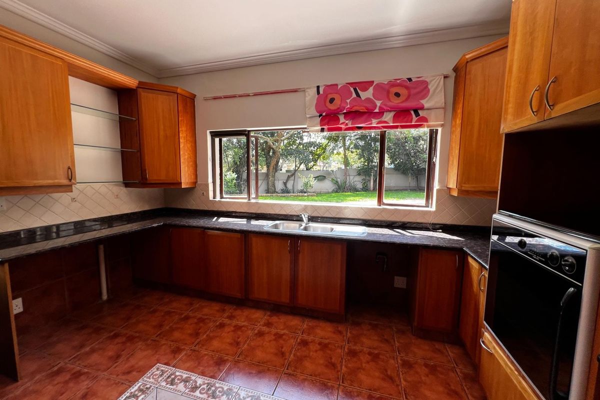 A functional kitchen featuring wooden cabinetry, dark granite countertops, a double basin sink, and a built-in oven, overlooking the rear garden.