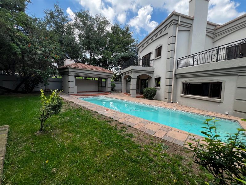 Rear exterior view featuring a rectangular swimming pool, paved surround, covered patio area, and a two-story house with balcony and chimney.