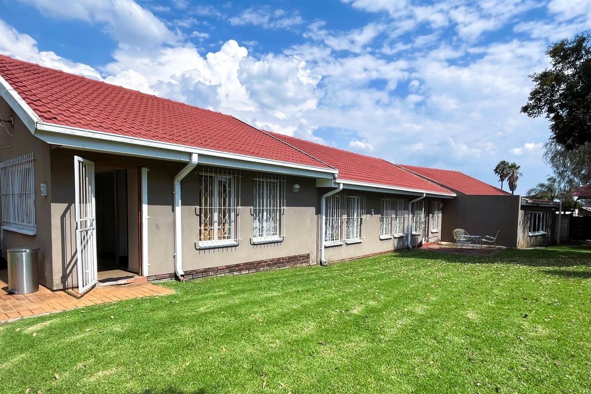 Rear view of the house featuring a red tiled roof, security bars on windows, and a well-maintained lawn with a small paved patio area.