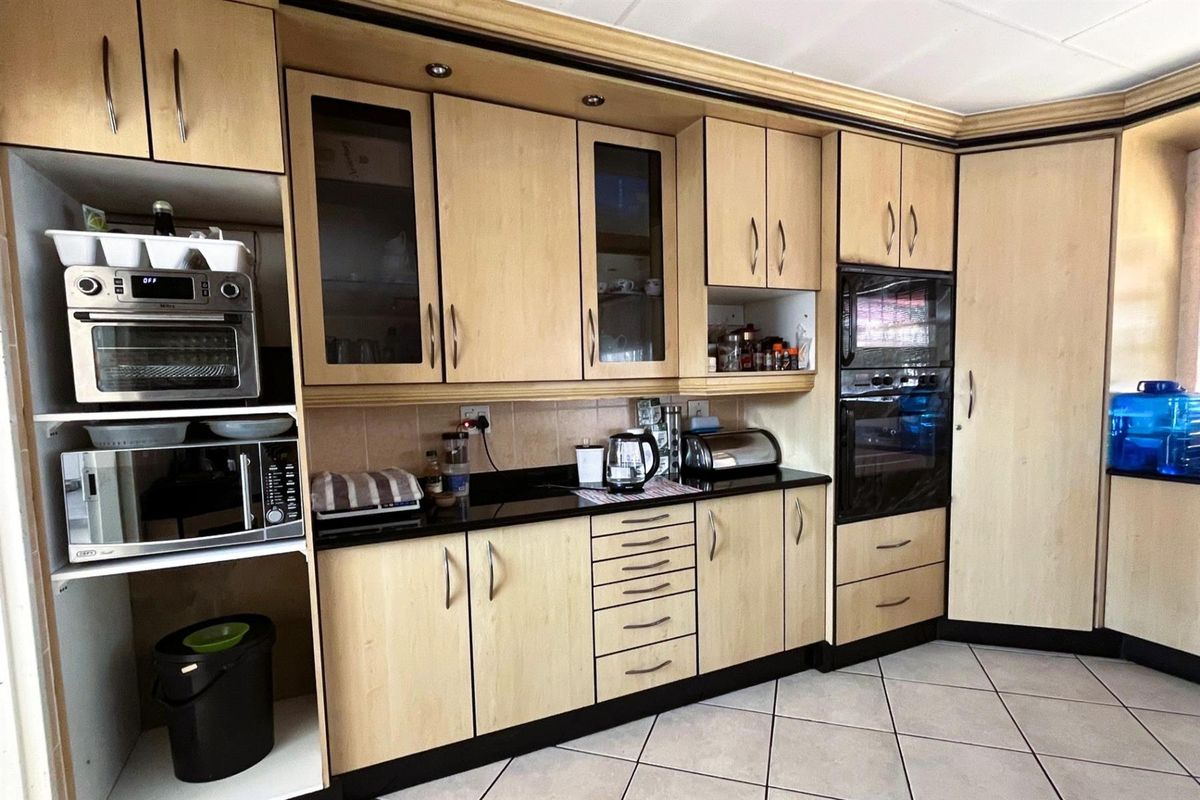 A functional kitchen featuring light wood-finish cabinetry, black granite countertops, built-in oven, and tiled flooring, offering a practical layout for daily meal preparation.