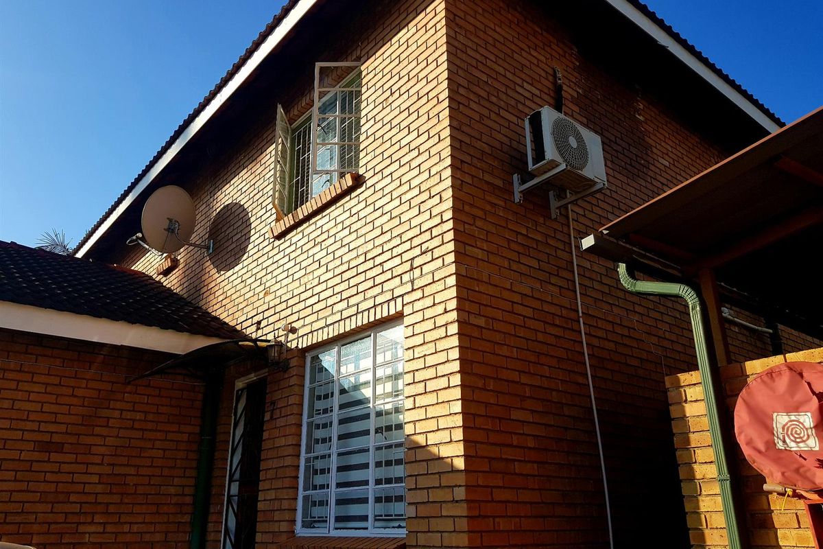 Rear exterior view of a double-story face brick townhouse featuring an installed air conditioning unit, security bars on windows, and tiled roofing.
