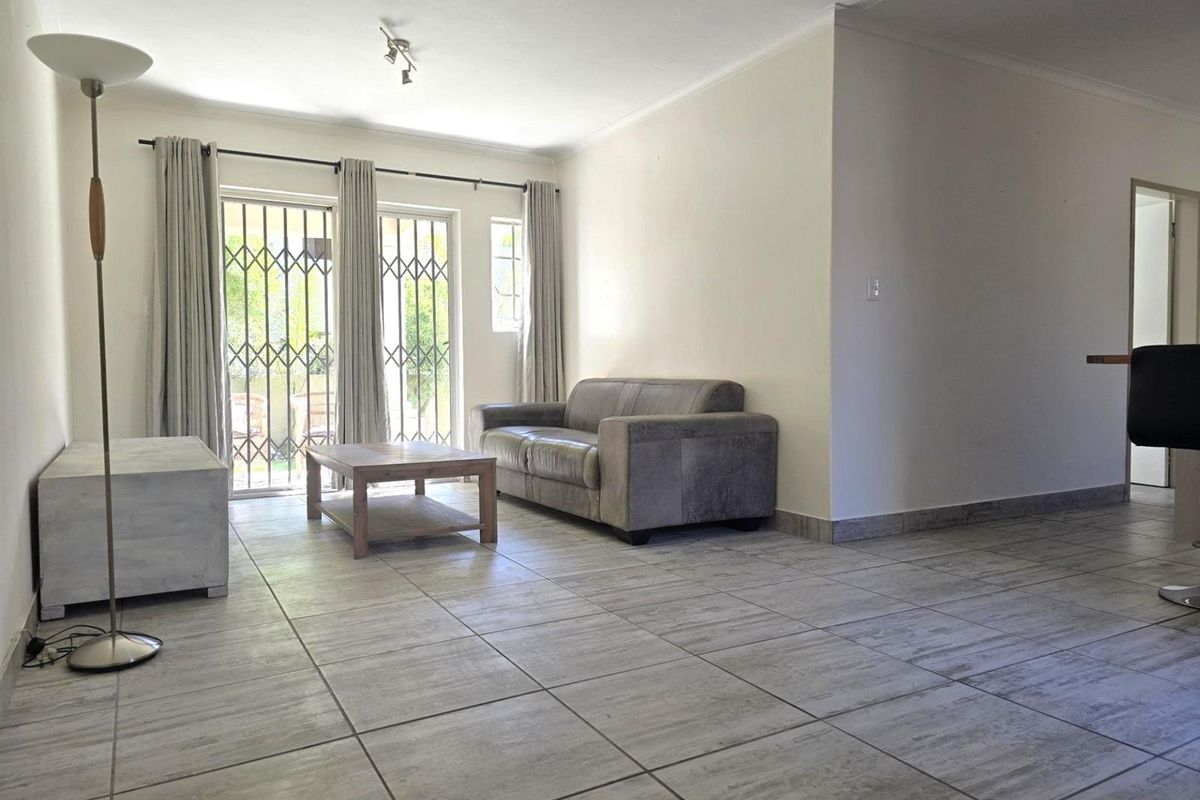 A bright living area featuring neutral floor tiles, sliding glass doors with security gates, and access to an outdoor space.