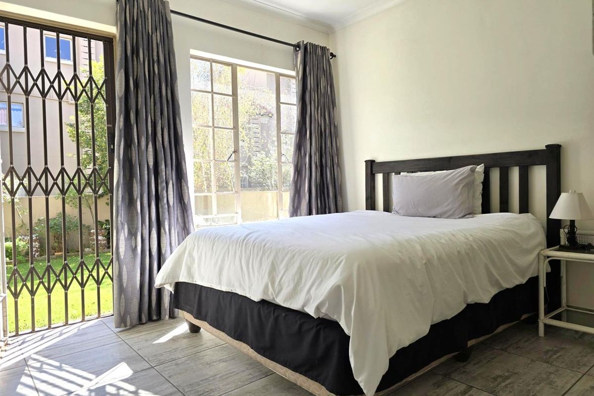 A bedroom featuring tiled flooring, large windows, and a security gate providing direct access to the outdoor area.
