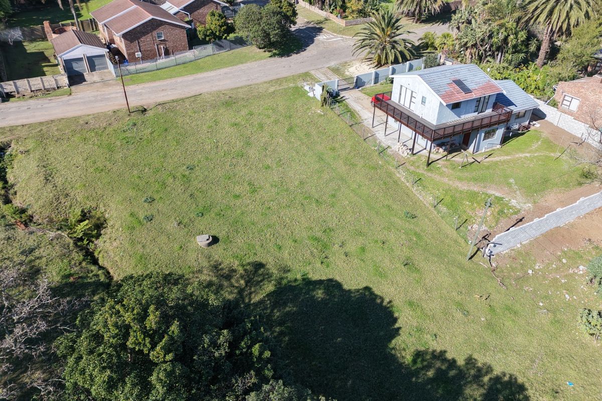Aerial view of a residential vacant land plot featuring established lawn, perimeter fencing, and mature trees, adjacent to an existing dwelling.