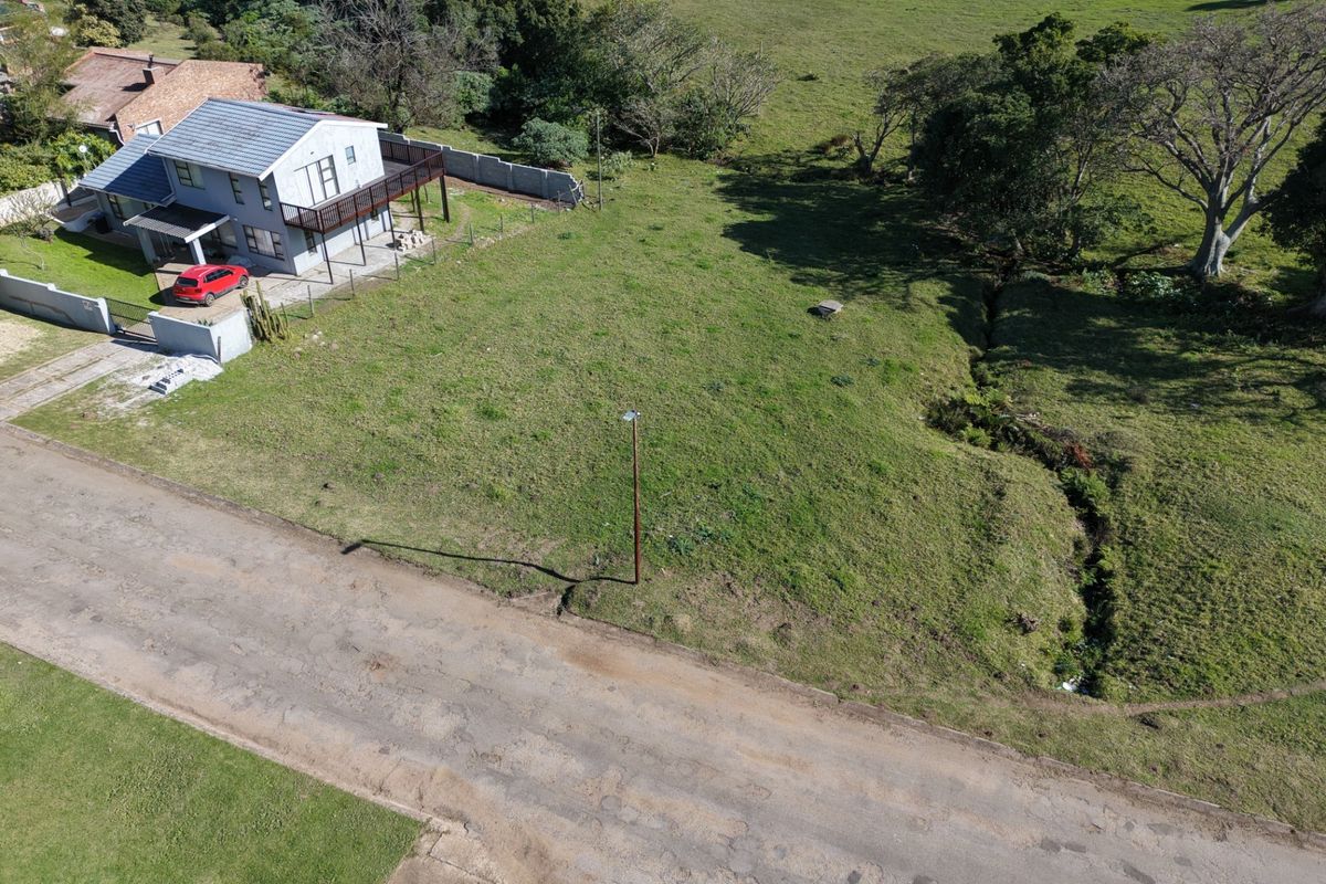 An aerial view of a vacant residential plot featuring natural grass cover, a drainage ditch, and existing boundary fencing.