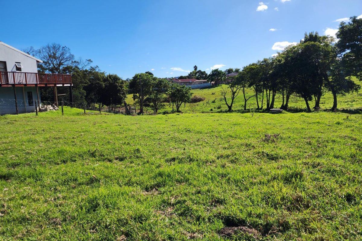 A view of the vacant residential land featuring open grassy terrain, mature trees, and a partial view of an adjacent property's elevated deck.