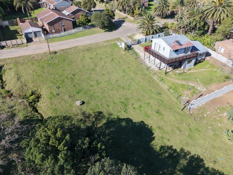Aerial view of a residential vacant land plot featuring established lawn, perimeter fencing, and mature trees, adjacent to an existing dwelling.