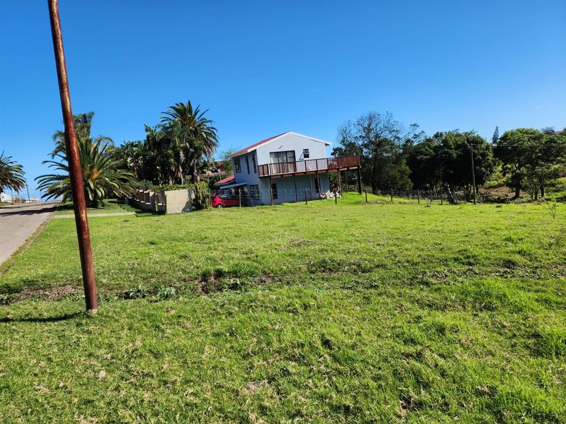 A view of a residential property featuring a two-story house with a raised wooden deck, situated on a large, open grassy plot.