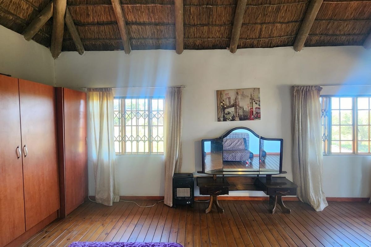 Spacious bedroom featuring a traditional thatched roof with exposed timber rafters, warm timber flooring, and built-in wardrobe storage.