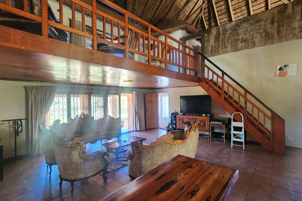 Spacious living area featuring a high thatched ceiling, a mezzanine level with wooden balustrades, tiled flooring, and an exposed stone feature wall.