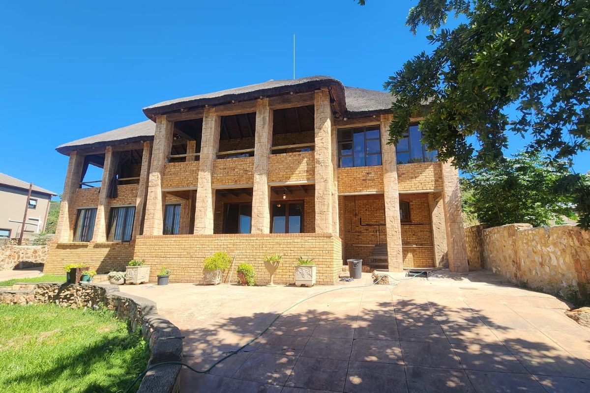 Rear view of a double-story face brick house featuring a traditional thatched roof, stone pillars, and a spacious paved patio area.