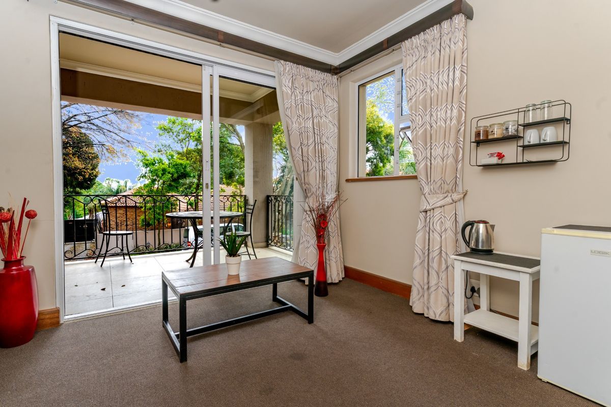A living area featuring sliding glass doors that open onto a covered balcony with wrought iron railings and garden views.