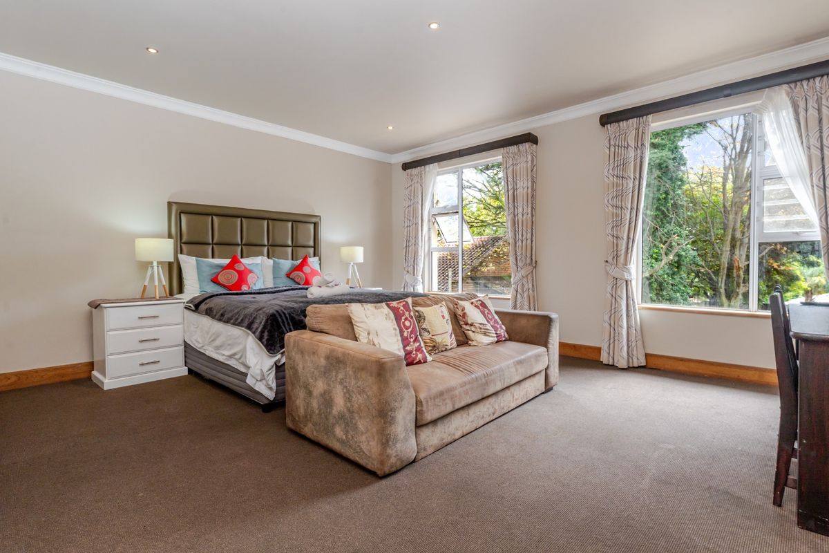 Spacious bedroom featuring neutral wall tones, plush carpeting, crown molding, and large windows providing natural light and garden views.