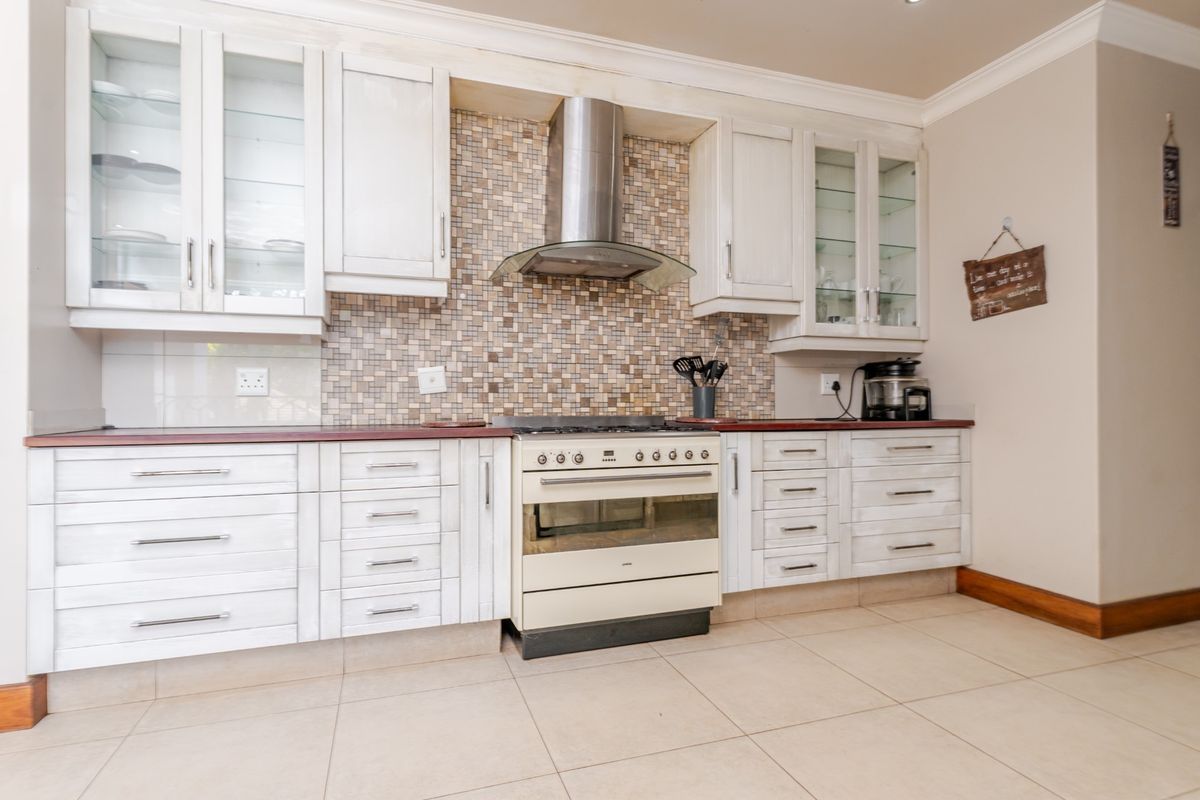 A functional kitchen featuring white cabinetry, a mosaic tile backsplash, and a stainless steel extractor fan with a freestanding oven.