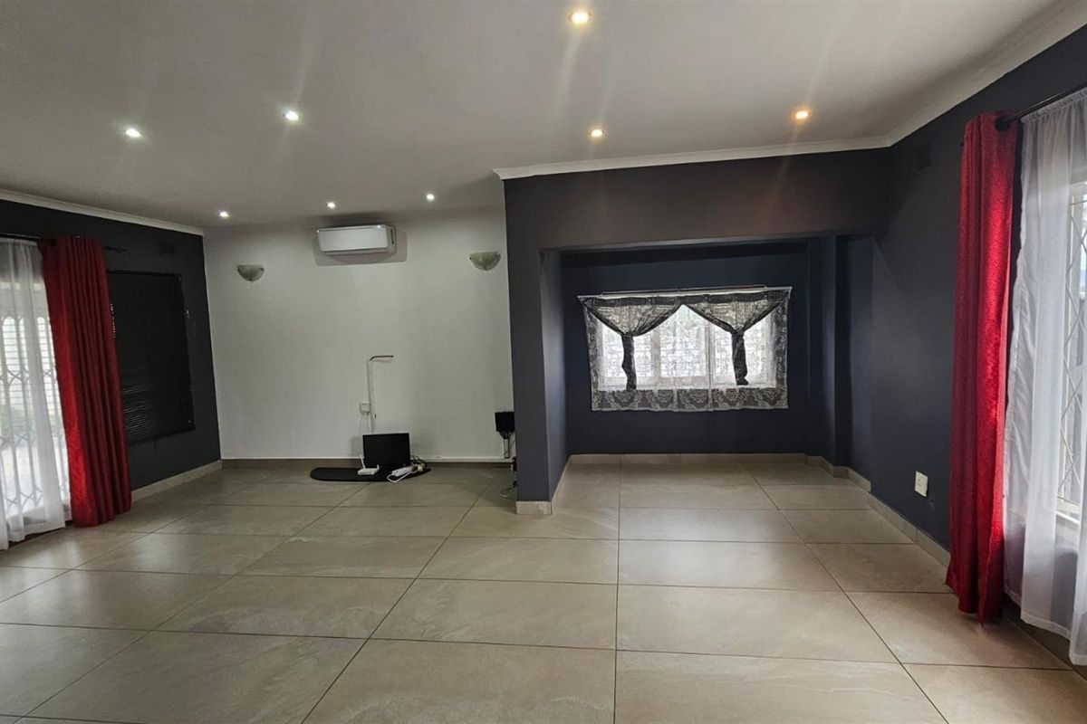 Spacious living area featuring large format floor tiles, recessed downlighting, and a wall-mounted air conditioning unit.