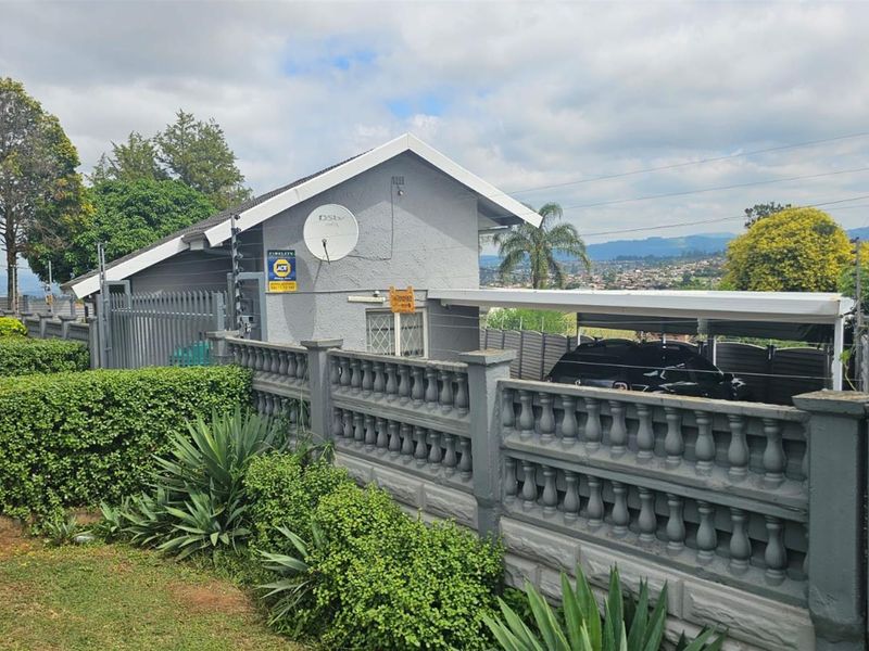 Exterior view of the property featuring a grey facade, a carport, and a decorative concrete boundary wall with integrated security fencing.