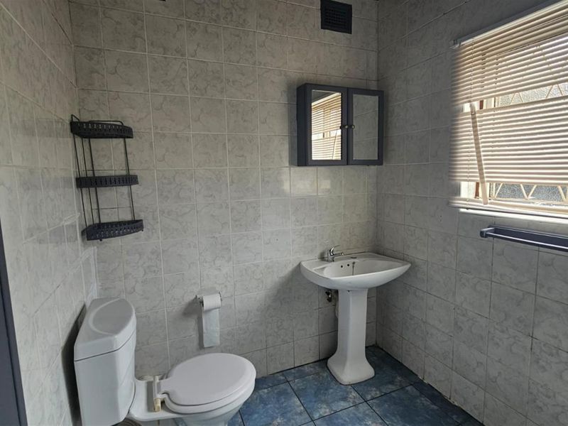 A functional bathroom featuring a pedestal basin, toilet, and full-height wall tiling, requiring cosmetic updates to modernize the space.