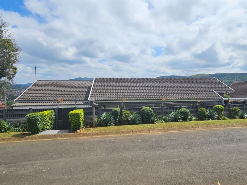 Street view of the property featuring a tiled roof, perimeter wall with electric fencing, and established garden landscaping.