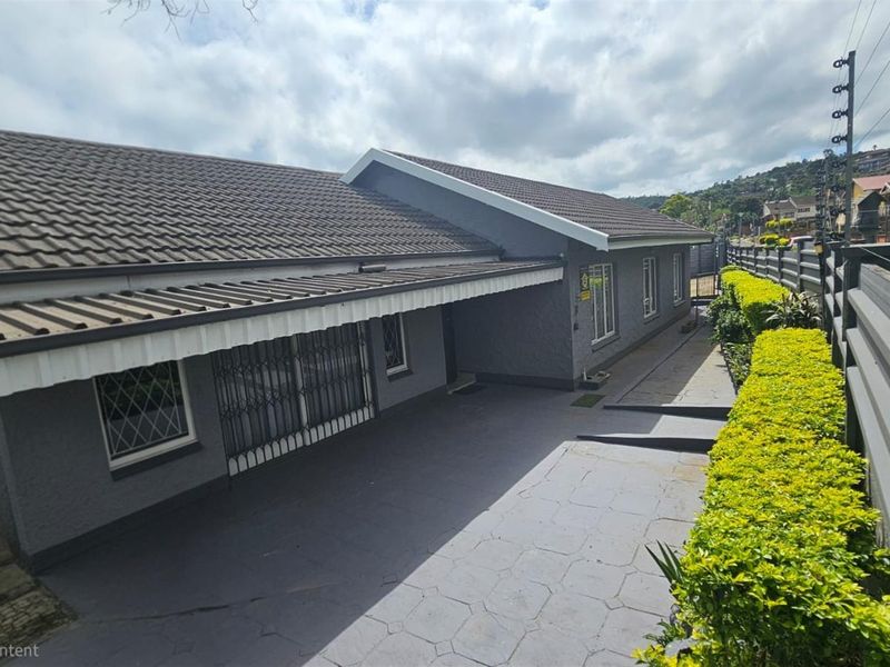 A well-maintained exterior view of the house featuring a paved driveway, covered patio area, and neatly landscaped garden hedges along the boundary fence.