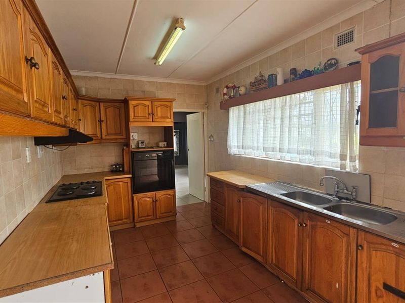 A functional kitchen featuring traditional timber cabinetry, tiled splashbacks, a built-in oven, and a double-basin sink with a window view.