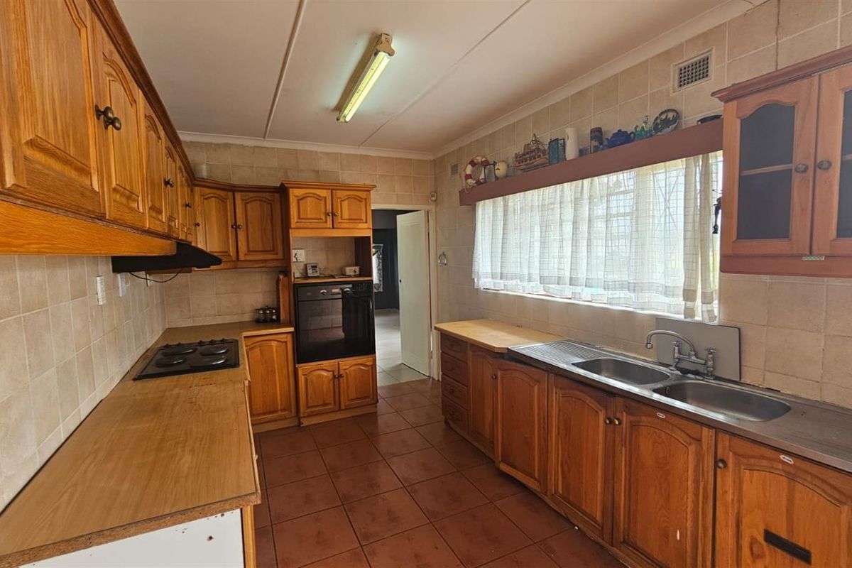 A functional kitchen featuring traditional timber cabinetry, tiled splashbacks, a built-in oven, and a double-basin sink with a window view.