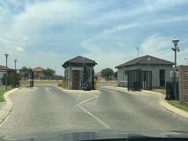 The entrance to the residential estate features a security gatehouse, boom gates, and paved driveway access.