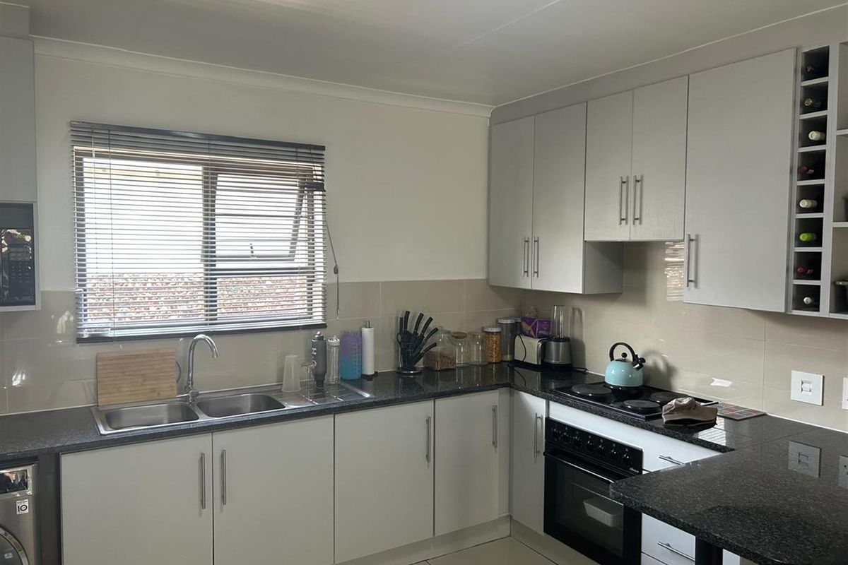 A functional kitchen featuring granite countertops, built-in cabinetry, a double sink, and integrated oven and hob, complemented by tiled flooring and neutral finishes.