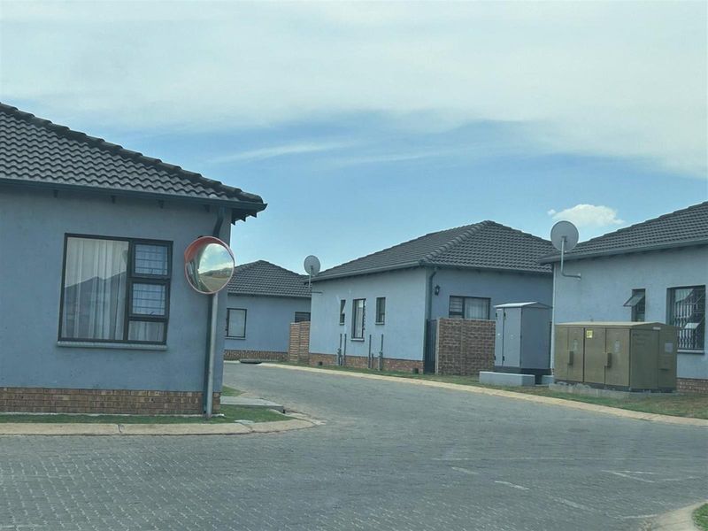 A street-level view of a residential complex featuring multiple detached houses with tiled roofs, paved driveways, and exterior utility infrastructure.