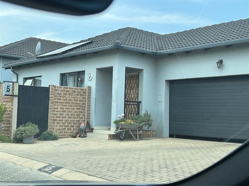 Front elevation of a single-story house featuring a paved driveway, integrated garage, tiled roof with solar panels, and a secure gated entrance.