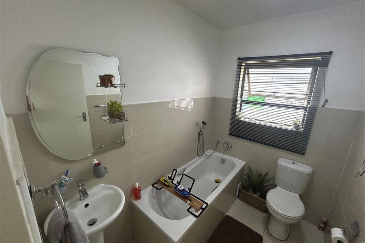 A functional bathroom featuring a pedestal basin, built-in bathtub with shower mixer, and a standard toilet with neutral wall and floor tiling.