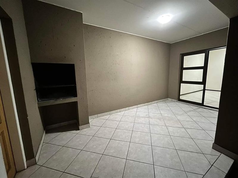 An empty living area featuring tiled flooring, a built-in braai, and a sliding glass door providing access to the exterior.