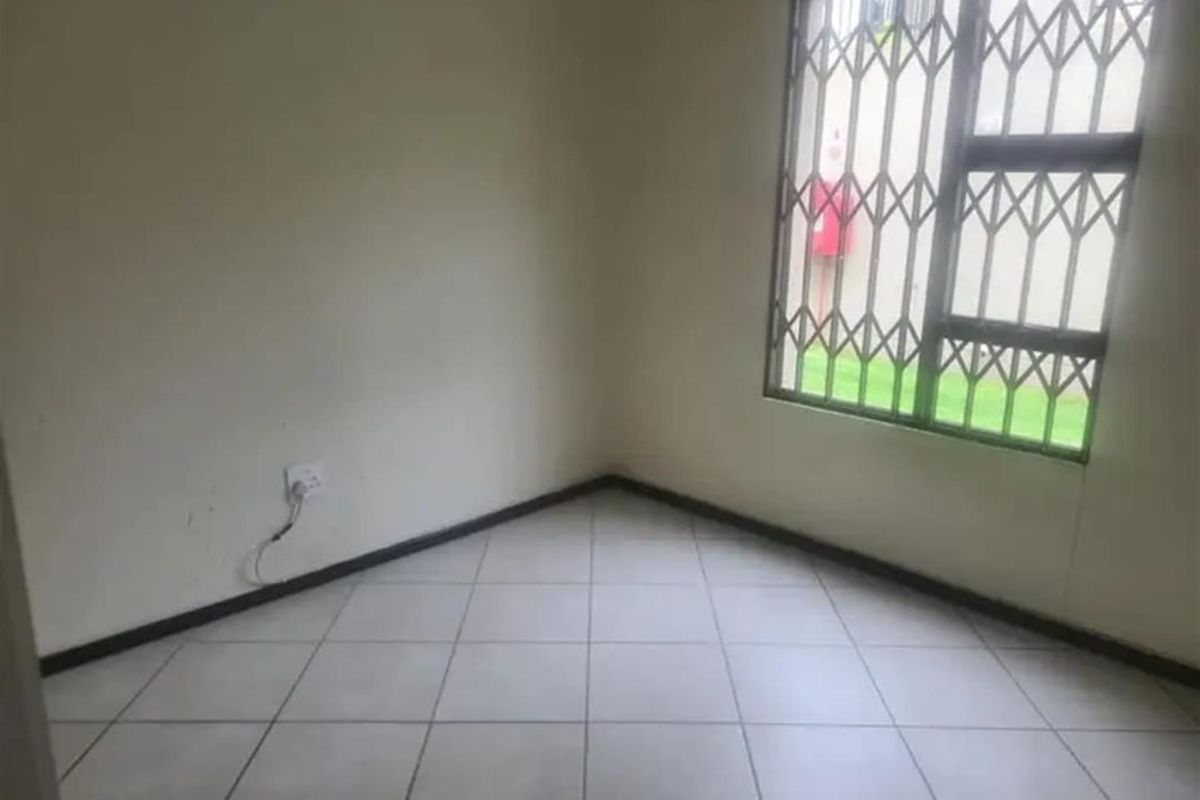 An empty bedroom featuring tiled flooring and a window fitted with a security gate, offering a blank canvas for potential interior design.