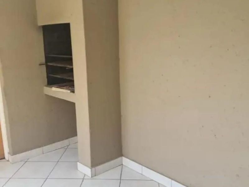 An empty living area featuring tiled flooring and a built-in indoor braai fireplace, ready for personalization.