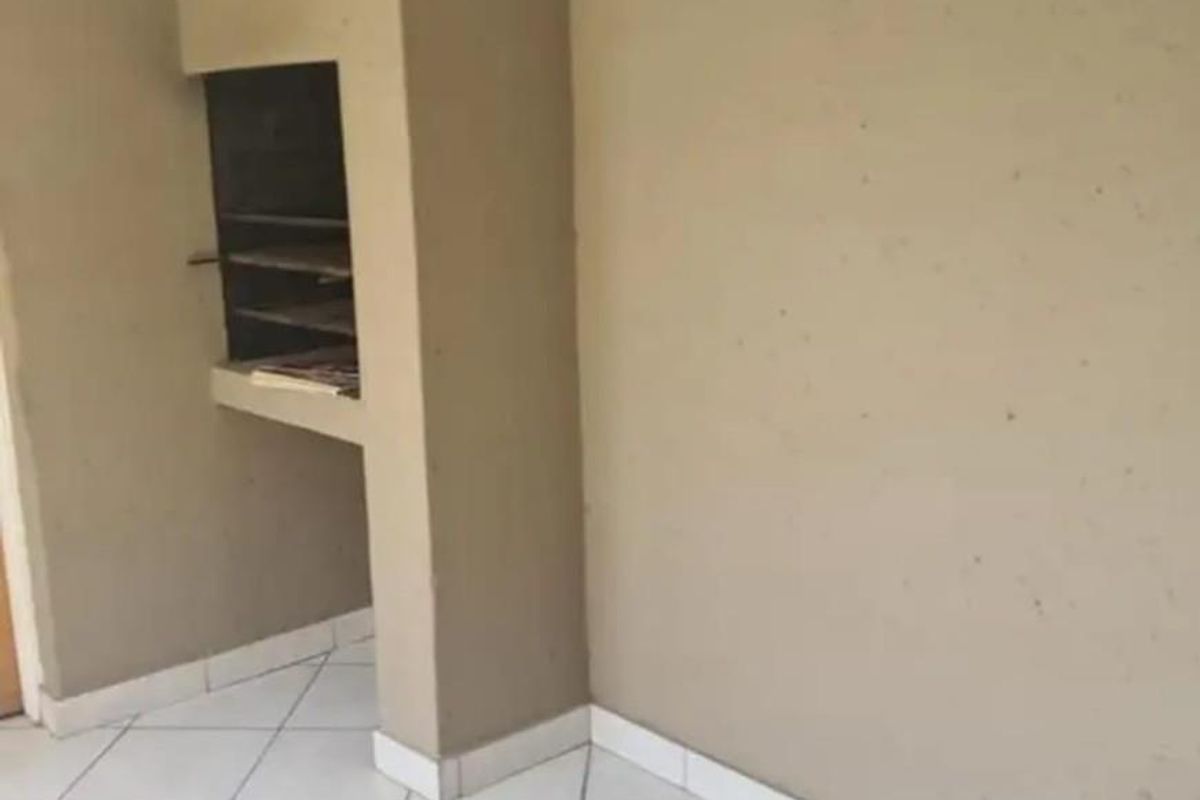 An empty living area featuring tiled flooring and a built-in indoor braai fireplace, ready for personalization.
