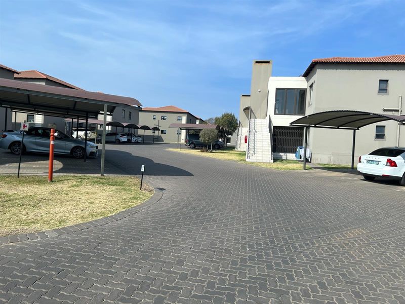 Exterior view of a townhouse complex featuring paved driveways, covered parking carports, and multi-story residential units with external staircases.