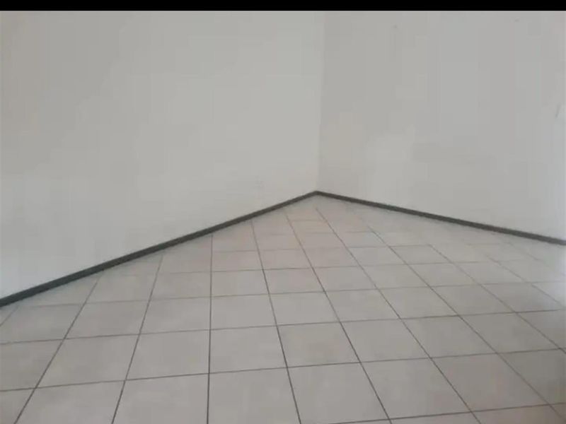 An empty living area featuring neutral tiled flooring and plain walls, providing a blank canvas for interior design.
