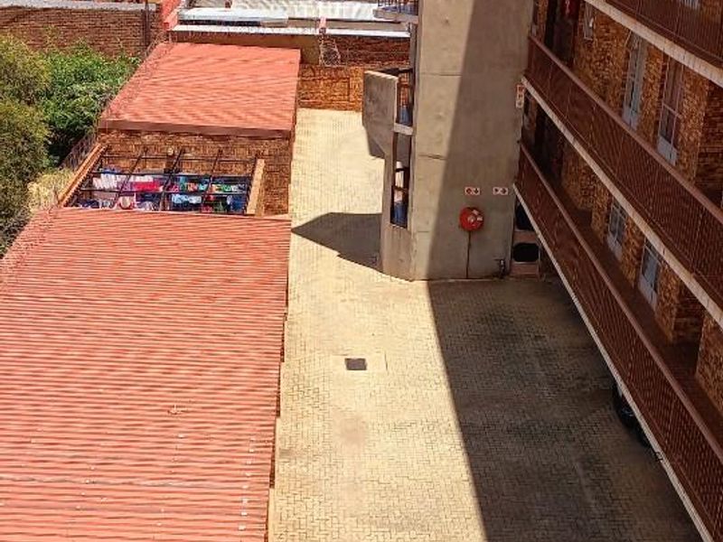 An elevated view of the apartment complex exterior, showing the brick facade, metal balconies, and paved ground level area.