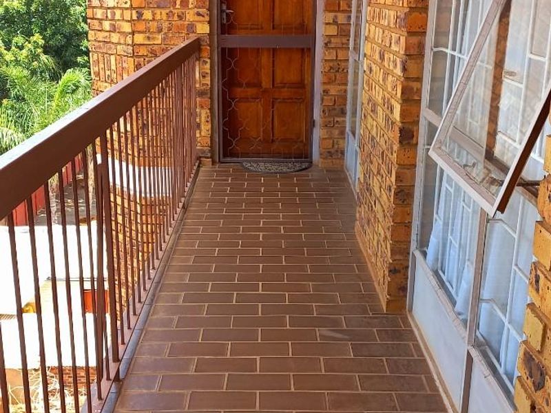 A covered balcony featuring exposed brick walls, tiled flooring, and metal safety railings, providing an outdoor transition space for the apartment.