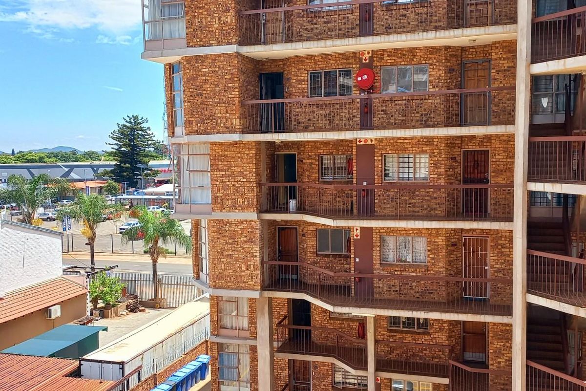 Exterior view of a multi-story apartment building featuring face-brick facade, open-air walkways, and metal security railings.