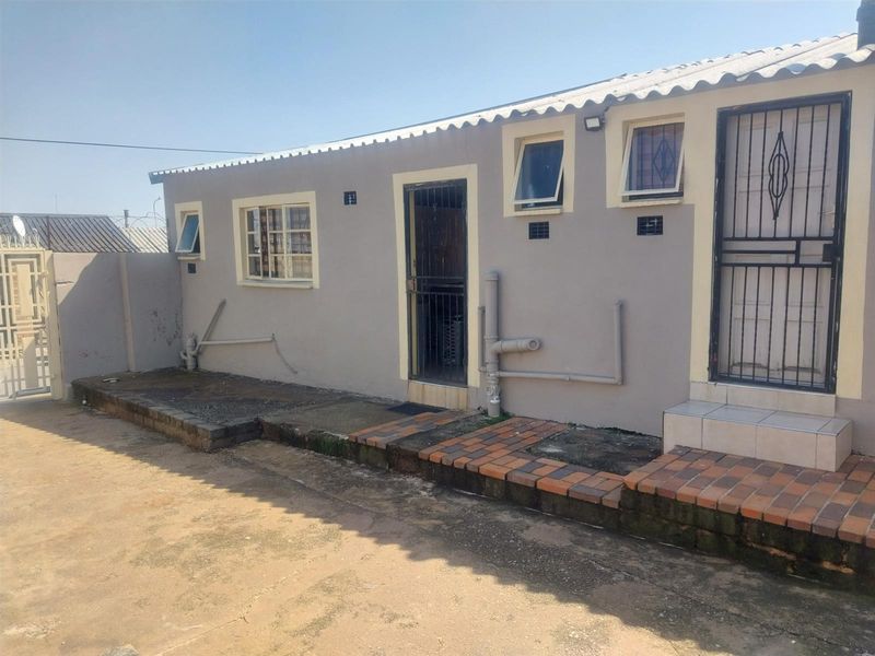 Rear exterior view of the cottage featuring security gates, casement windows, and exposed plumbing, with paved access area.