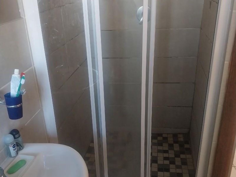 A functional bathroom featuring a shower enclosure with tiled walls and a pedestal basin, presenting a standard, lived-in condition.