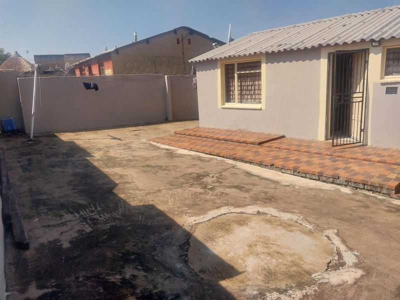 Rear exterior view of the cottage featuring a tiled patio area and a concrete yard with perimeter walling.