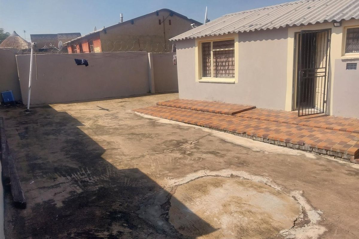 Rear exterior view of the cottage featuring a tiled patio area and a concrete yard with perimeter walling.