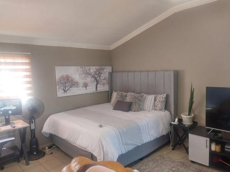 A comfortable bedroom featuring tiled flooring, coved ceiling details, and neutral wall tones, providing a functional and well-lit sleeping space.