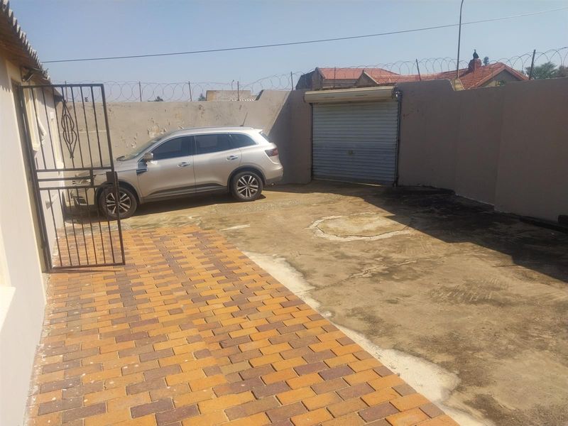 Rear exterior area featuring a paved driveway, perimeter wall with security razor wire, and a roller shutter garage door.
