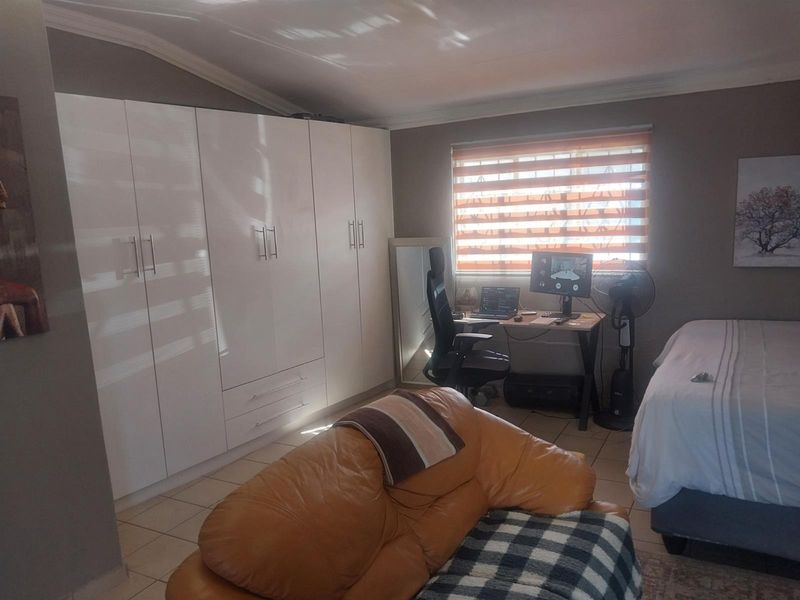 A well-maintained bedroom featuring extensive built-in cupboards, tiled flooring, and modern roller blinds, offering a functional and comfortable living space.