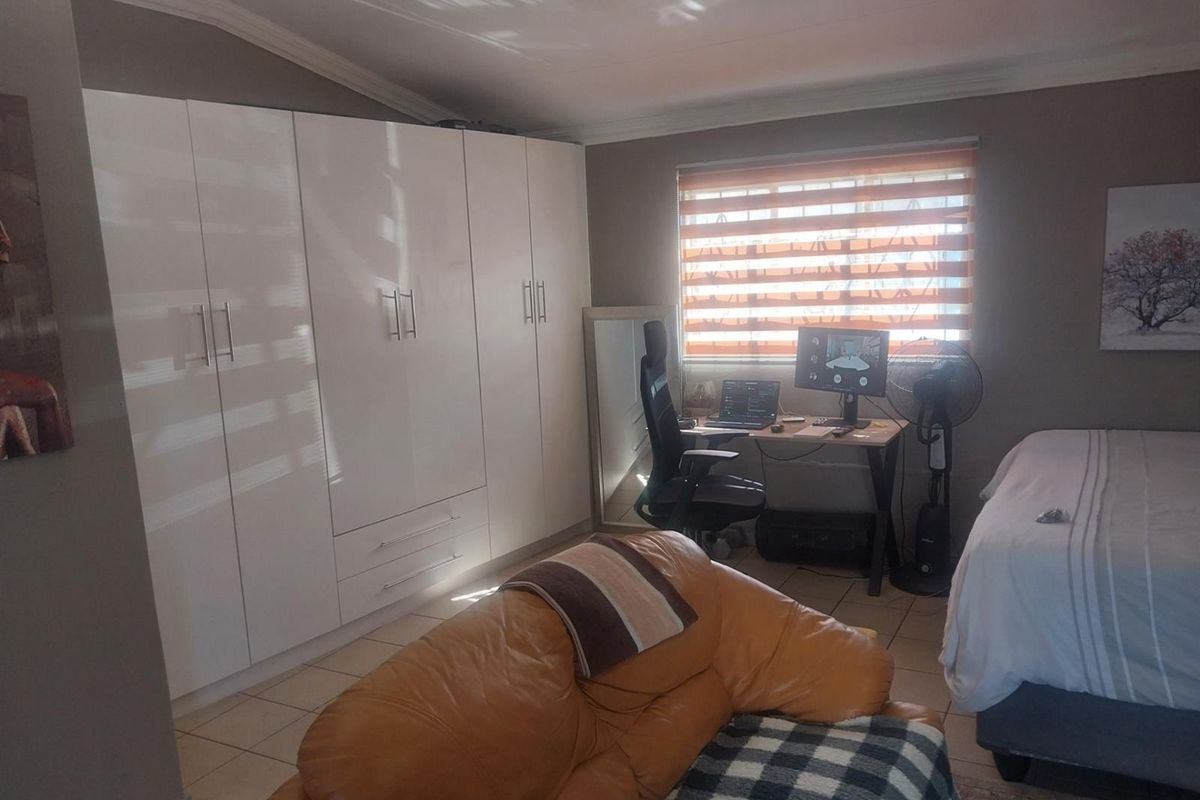 A well-maintained bedroom featuring extensive built-in cupboards, tiled flooring, and modern roller blinds, offering a functional and comfortable living space.